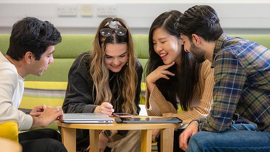 Group of postgraduate students sat around a table looking at an ipad