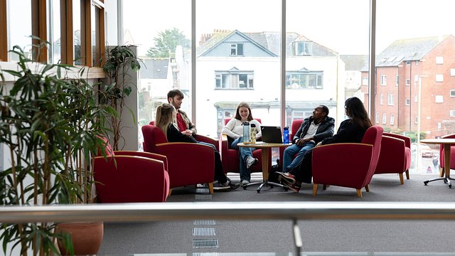 A group of students sitting around a small table in front of a large window.
