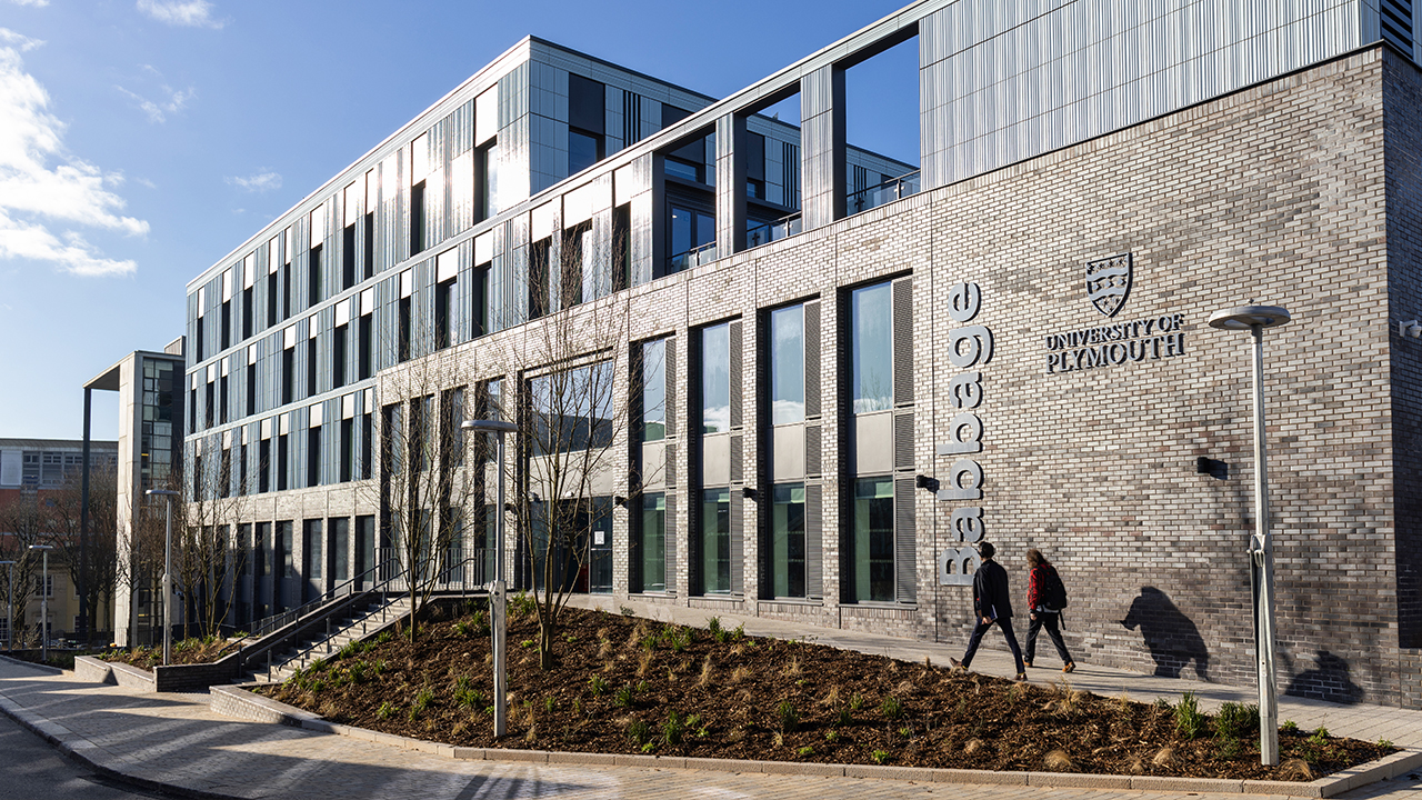 Babbage building on a sunny day with blue skies, two people entering the building.