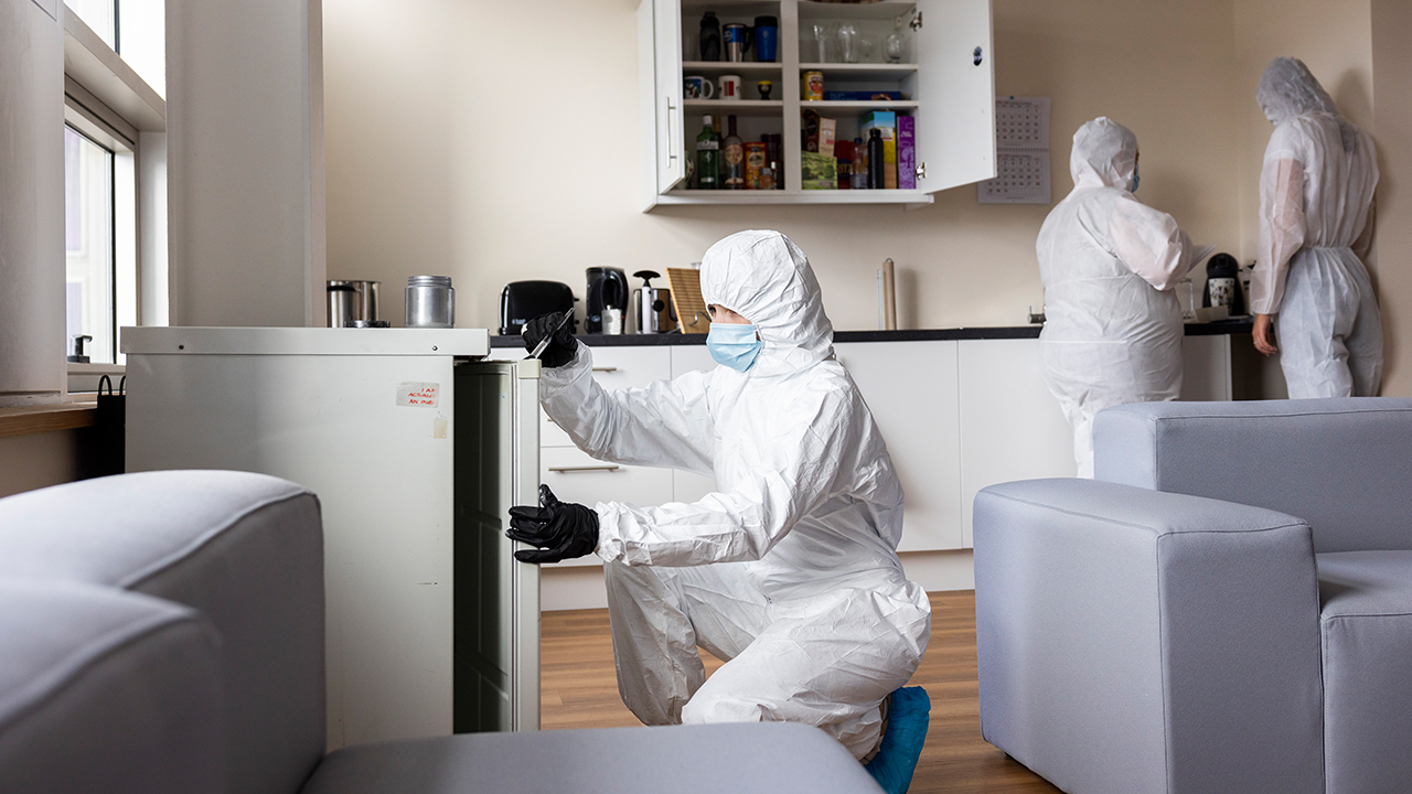 Criminology student dusting for prints in a crime scene, during a simulation at the crime suite 'murder house' 