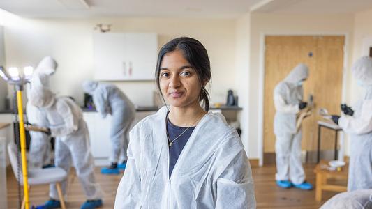 Sidney De Souza - Criminology Student poses in the murder house while students work around her